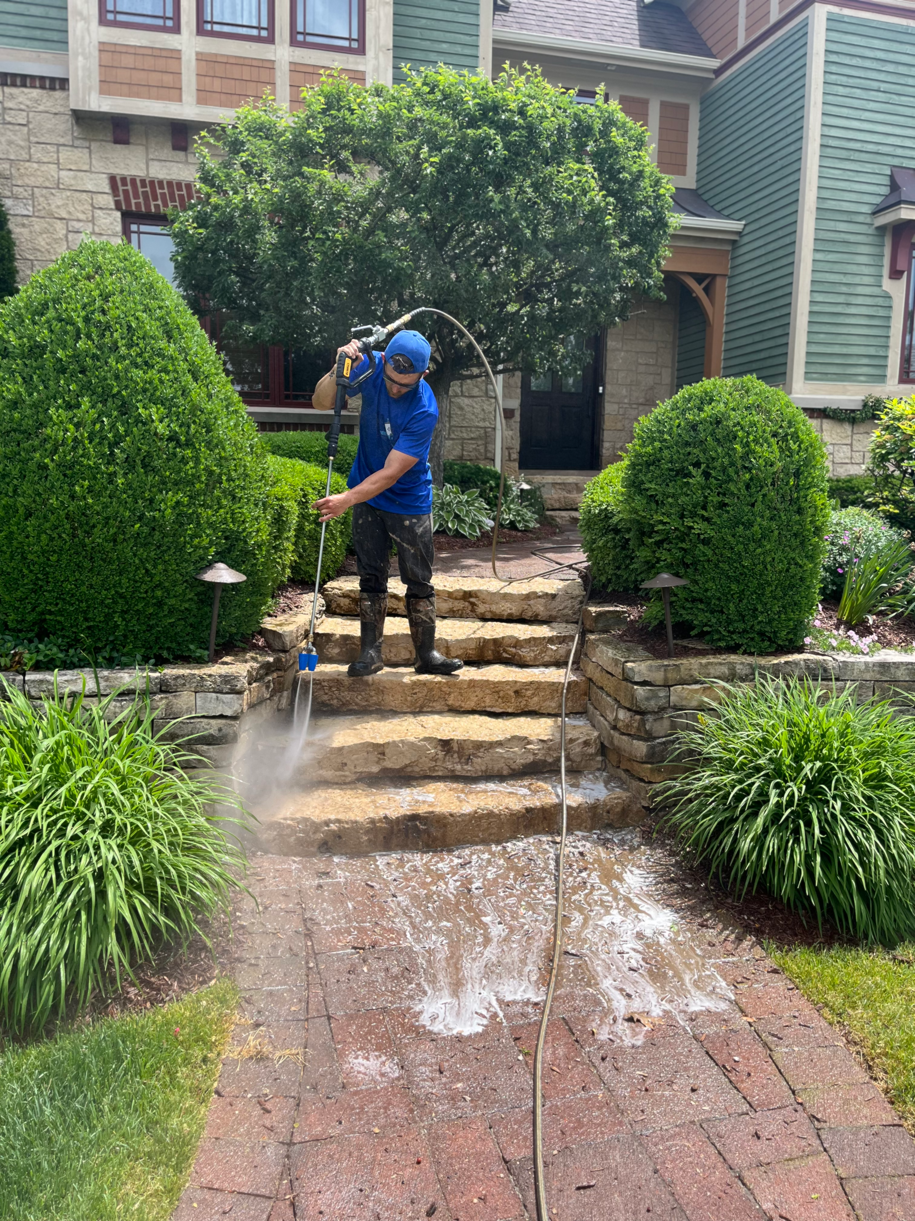 A man in a blue uniform power washing stone steps and a brick pathway